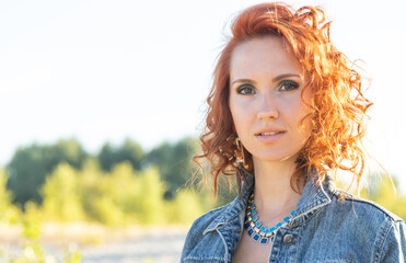 Portrait of a red haired beautiful woman in a denim jacket on a background of nature.