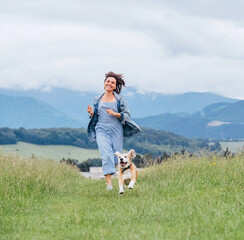 Smiling running beagle dog portrait with tongue out and happy owner female jogging by the mounting meadow grass path. Walking in nature with pets, happy healthy active people lifestyle concept image.