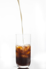 milk being poured into a black iced coffee 