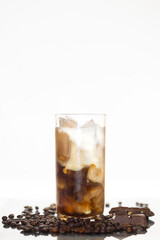 cloudy iced coffee in a glass surrounded by coffee beans and chocolate 