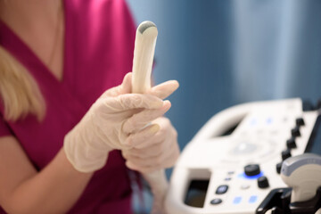 Gynecologist places ultrasound probe cover on a transvaginal ultrasound scanner for vaginal examination of a woman using an ultrasound machine. Ultrasound of the pelvic organs. Shooting close-up.