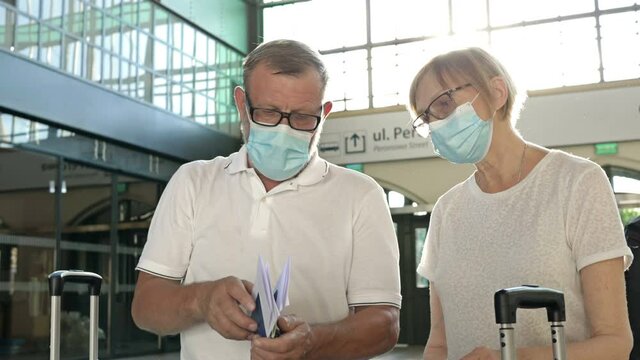 An elderly couple is waiting for their flight in the waiting room. Medical masks on their faces. Travel, tourism during the coronavirus epidemic.