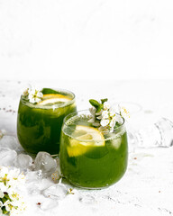 Green basil lemonade with yellow lemon and  white flowers on white painted background