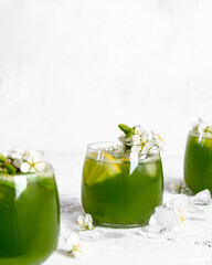 Green basil lemonade with yellow lemon and  white flowers on white painted background