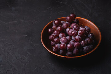 Fresh ripe grape berries in brown wooden bowl on dark stone background, angle view
