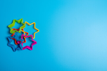 Four multi-colored plastic cookie cutter for making cookies in the shape of stars on a blue...