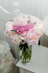 Beautiful white and pink peonies in a glass vase on the bedside table in the bedroom. Womens Day greetings concept