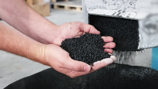 Man holding plastic black gray granulated crumb pouring in the bag