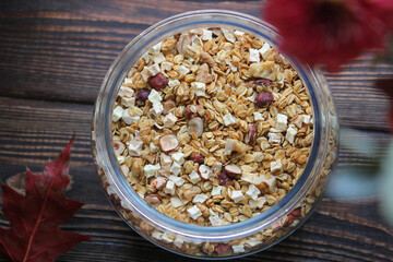 Granola for breakfast and snack, baked muesli with hazelnuts and apple in a glass jar on a dark wooden background. View from above