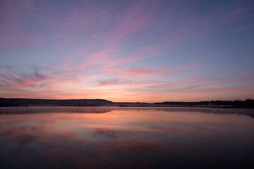 Fototapeta na wymiar Pink sky over the lake with haze above the water in the morning before dawn