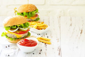 Delicious homemade burgers with cutlet, cheese, bacon, tomatoes and french fries on a wooden table. Copy space.