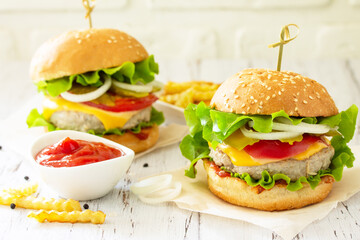 Delicious homemade burgers with cutlet, cheese, bacon, tomatoes and french fries on a wooden table.