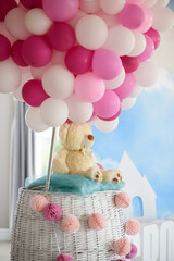 Stylish and modern decoration for a children's party with a toy teddy bear in a basket and white, pink and raspberry balloons