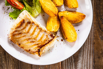 Fish dish - fried cod fillet with potatoes and vegetable salad on wooden table