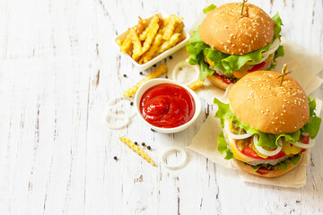 Delicious homemade burgers with cutlet, cheese, bacon, tomatoes and french fries on a wooden table. Copy space.