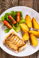 Fish dish - fried cod fillet with potatoes and vegetable salad on wooden table