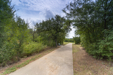 A concrete path in a Texas urban nature reserve on a sunny September day.