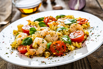 Pasta with prawns and vegetables highly seasoned on wooden table