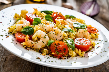Pasta with prawns and vegetables highly seasoned on wooden table