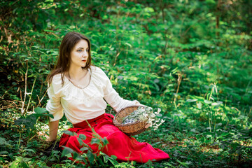 Beautiful lady sitting and holding a basket of flowers in the forest