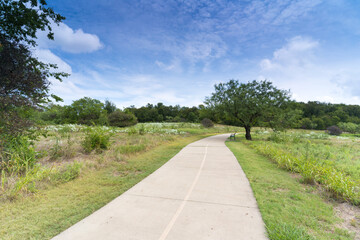 A concrete path in a Texas urban nature reserve on a sunny September day.