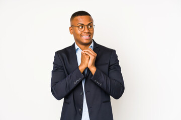 Young business latin man isolated on white background keeps hands under chin, is looking happily aside.