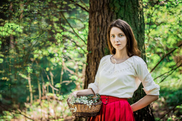 Beautiful lady holding a basket of flowers in the forest