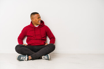 Young latin man sitting on the floor isolated shouting towards a copy space
