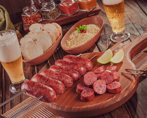 Grilled Sausage skewer on wooden board with beer, bread and farofa - Brazilian barbecue
