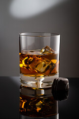 A glass of Kentucky Bourbon on rocks and piece of chocolate candy  placed on black reflection surface with gray background