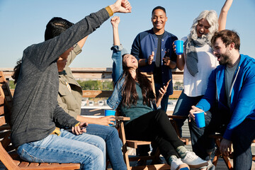 Group of young co-workers hanging out on rooftop patio having a drink and celebrating achievement reached on cell phone 