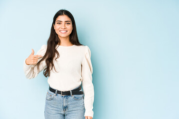 Young indian woman isolated on blue background person pointing by hand to a shirt copy space, proud and confident