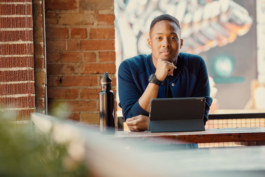 Portrait of mixed race young man working on a tablet at an outdoor cafe, looking at camera. 
