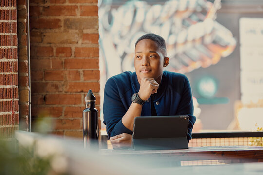 Portrait of mixed race young man working on a tablet at an outdoor cafe, looking off camera. 