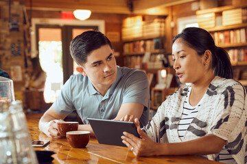 Young man and woman sitting at counter in cafe bookstore looking at tablet