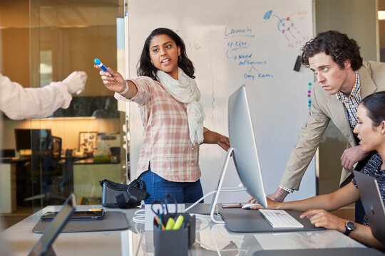 Co-Workers talking at computer in office while woman is working on dry erase board with flowchart 