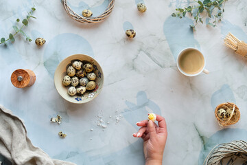 Obraz na płótnie Canvas Zero waste Easter background on marble table. Quail Easter eggs and natural Spring decorations, twigs and eucalyptus. Hand with peeled egg. Cofee in bamboo cup.