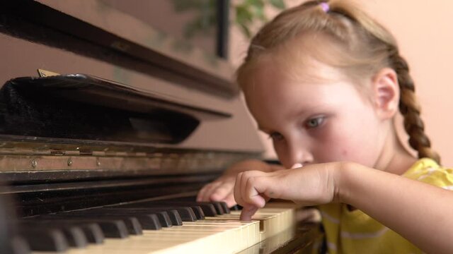 The child is tired of learning a music lesson. A pretty girl put her head on the piano keys. A little girl plays the piano in a music class.4k