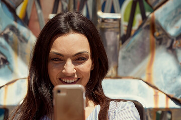 Young woman in front of chrome sculpture using mobile phone to take selfie 