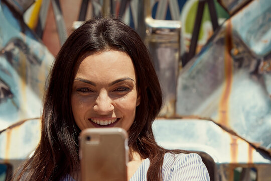 Young woman in front of chrome sculpture using mobile phone to take selfie 