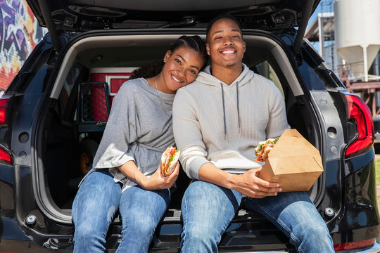 Portrait of young African American couple having impromptu picnic lunch in the back of their vehicle.