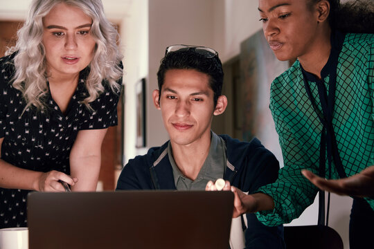 Group of young co-workers gathered around laptop computer looking at screen discussing project  