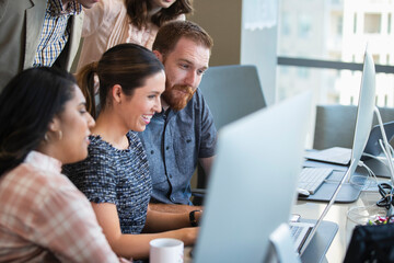 Young woman using laptop computer in conference room showing co-workers something on screen 
