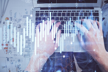 Double exposure of man's hands typing over laptop keyboard and forex chart hologram drawing. Top view. Financial markets concept.