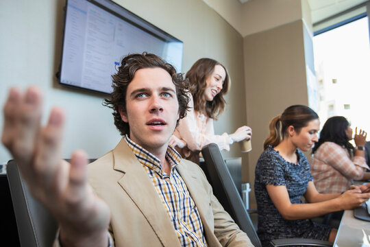 Young man having discussion in conference room with co-workers working in background 