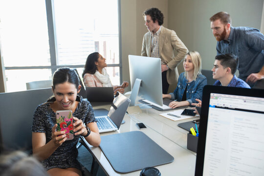 Woman taking picture with mobile phone, while colleagues work in background of conference room 