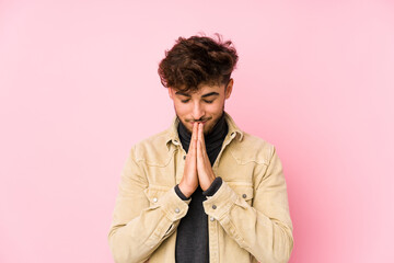 Young arabian man posing in a background isolated holding hands in pray near mouth, feels confident.