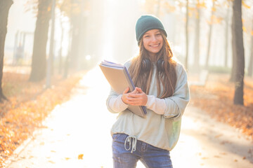 Happy school girl holding folders in autumn park