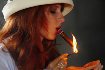 woman lit a match and lights a cigar.Elegant smoking woman. Portrait of a red-haired girl with a...