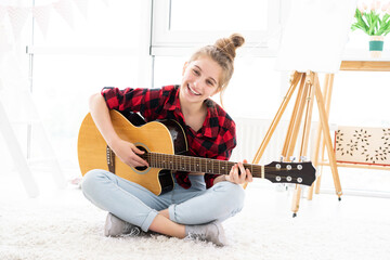 Happy teenage girl playing guitar in bright room